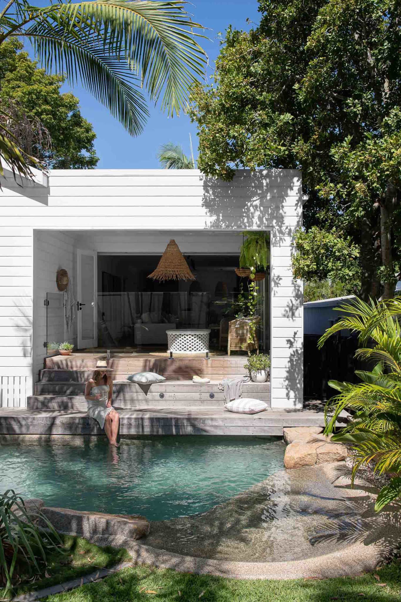 The Beach Society House exterior by the pool. Jordan's feet are dangling in the water while she relaxes by the pool.