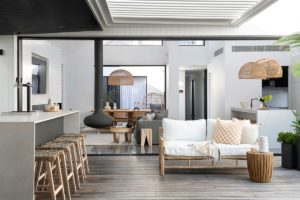 A cane lounge styled with a checkered cushion and throw and outdoor bar area.