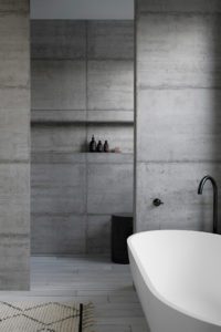 A concrete bathroom with a white tub.