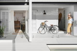 A lady in yellow pants with a hat stands at the front door near her bike.