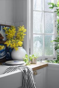 A kitchen window is open with yellow flowers in a vase sitting on the counter.
