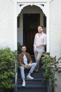 A couple stand and sit at the entrance of their home.