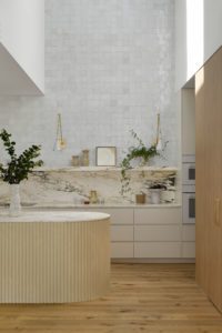 A modern kitchen with a rounded kitchen island with fluted edging, a marble backsplash, and styled open shelving.