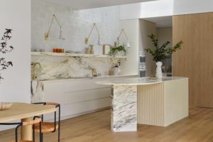 A modern kitchen with a rounded kitchen island with fluted edging, a marble backsplash, and styled open shelving.