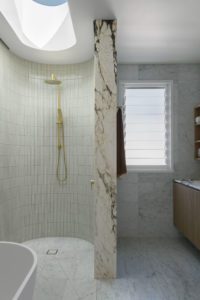A modern bathroom styled with marble and brass details with a skylight over a freestanding bathtub.