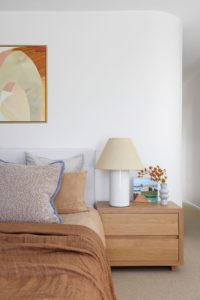 A modern bedroom styled with terracotta toned linen and ceramics on the bedside table.