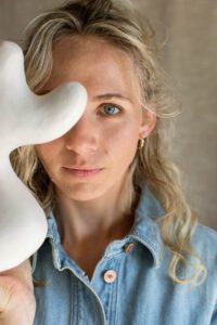 A close up of ceramic artist Tess Miller, one eye is covered by an organic shaped sculpture.