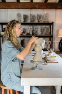 Tess sitting at her work bench moulding a vase.
