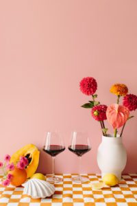 Two monogrammed wine glasses surrounded by flowers and fruit.