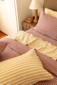 A close shot of a styled bed with Pinot Gingham and Yellow Stripe linen.