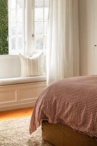 The end of a bed styled with Pinot Gingham and Yellow Stripe bed linen, looking onto a sun window.