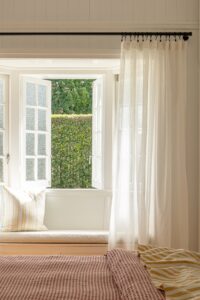 A sunlit window seat with cushion and soft curtains.