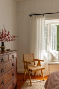 A rattan chair and dresser styled with flowers, overlooking a sun window.