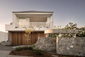 A street view of a modern architectural home, featuring white metal cladding, oak panels, and stonework.