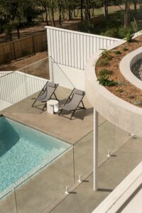 Looking down on a modern architectural pool area, featuring concrete finishes and charcoal deck chairs.