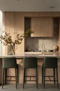 A light filled modern architectural kitchen with oak cabinets, brass finishes, and upholstered bench stools.