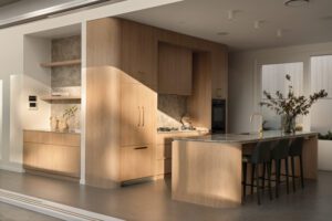 A light filled modern architectural kitchen with oak cabinets, brass finishes, and upholstered bench stools.