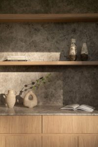 A modern architectural shelf made of grey marble and oak, featuring decorative books and handmade ceramic vases.