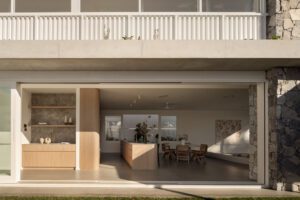 An outside view looking into a light-filled modern architectural home, featuring stonework, oak tones, and abstract art.