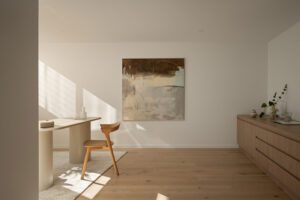 A modern and light filled home office decorated in a minimalistic style with abstract art and oak tones.