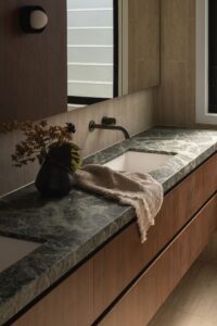 Marble bathroom bench top on walnut cabinetry with vase and hand towel on bench.