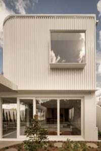 A side view of the exterior of a modern architectural home, featuring white metal cladding and glass sliding doors.