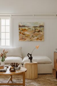 A new white James Lane couch styled with rattan and chocolate brown accents. A piece from local artist La Horton hangs on the wall.