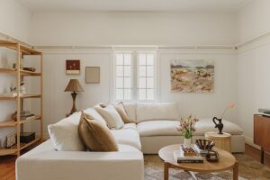 A new white couch in a renovated Queenslander living room. There are rattan and chocolate brown accents around the room. A piece from local painter La Horton hangs on the wall.