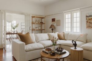 A new white couch in a renovated Queenslander living room. There are rattan and chocolate brown accents around the room. A piece from local painter La Horton hangs on the wall.