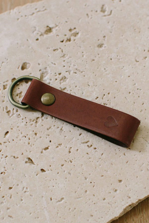 A tan keyring in tan leather on a travertine stone backdrop.