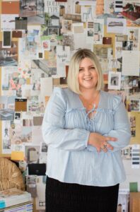 Hayley in a blue top standing in front of a pinboard.
