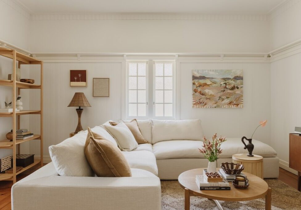 A new white couch in a renovated Queenslander living room. There are rattan and chocolate brown accents around the room. A piece from local painter La Horton hangs on the wall.